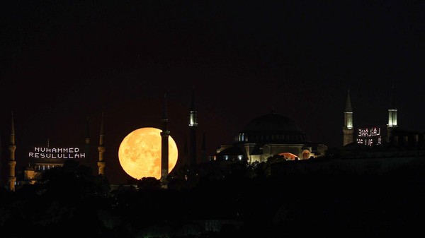 Penampakan bulan purnama yang tampak berada di antara Masjid Biru dan Hagia Sophia di Istanbul, Turki, Rabu (13/7/2022). (Ali Atmaca/Anadolu Agency/Getty Images).
