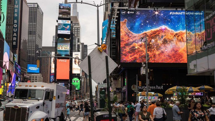 Potret Menakjubkan Galaksi dari Teleskop James Webb Mejeng di Times Square A person takes a video of the gians screens displaying images captured by The James Webb Space Telescope in Times Square on July 12, 2022 in New York. - Released one by one starting from 10:30 am Eastern (1430 GMT) at the Goddard Space Flight Center, the new images demonstrated the full power of the $10 billion observatory, which uses infrared cameras to gaze into the distant universe with unprecedented clarity. (Photo by Yuki IWAMURA / AFP) (Photo by YUKI IWAMURA/AFP via Getty Images)