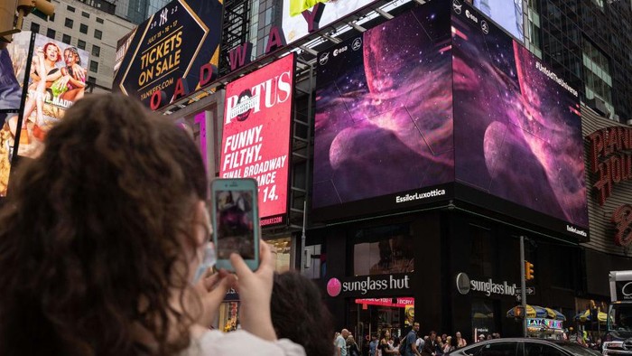 Potret Menakjubkan Galaksi dari Teleskop James Webb Mejeng di Times Square A person takes a video of the gians screens displaying images captured by The James Webb Space Telescope in Times Square on July 12, 2022 in New York. - Released one by one starting from 10:30 am Eastern (1430 GMT) at the Goddard Space Flight Center, the new images demonstrated the full power of the $10 billion observatory, which uses infrared cameras to gaze into the distant universe with unprecedented clarity. (Photo by Yuki IWAMURA / AFP) (Photo by YUKI IWAMURA/AFP via Getty Images)