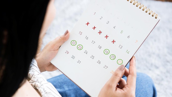 Asian woman hand holding calendar counting the date and checking her menstrual cycle planning for ovulation.