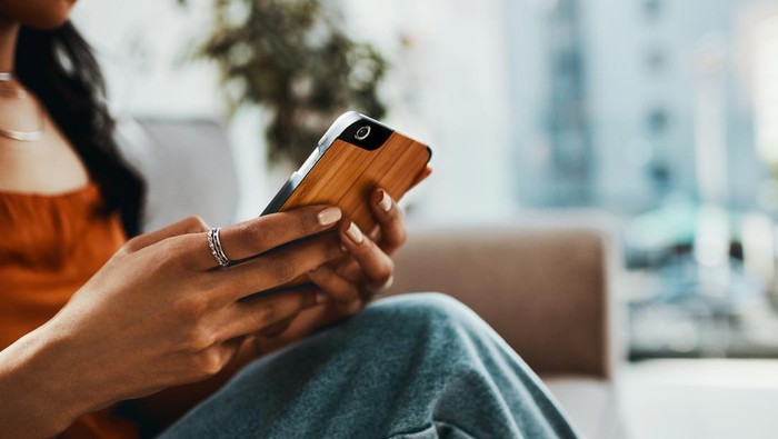 Cropped shot of a woman using a smartphone while relaxing on the sofa at home