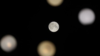 Penampakan Purnama Rusa atau Buck Moon di sela-sela lampu jalanan yang terlihat di langit Milan, Italia, Rabu (13/7/2022) malam waktu setempat. (AP Photo/Luca Bruno).