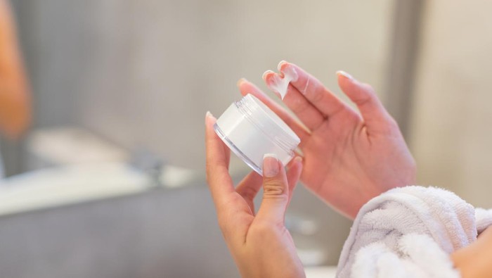Hand holding a facial cream jar and taking cream out with fingers