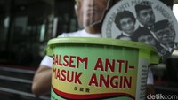 Seorang lagi tampak memegang benda menyerupai koin dengan gambar lima orang Dewas KPK di dalamnya. Dia juga membawa sebuah ember bertuliskan Balsem Anti-Masuk Angin. Aroma Anti-Gratifikasi.