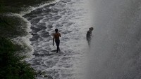 Aliran air yang tumpah keluar bendungan dimanfaatkan warga untuk berenang dan main air.