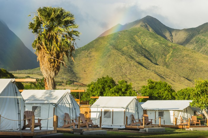 Canvas glamping bell tents in a green field with walkway at mountain view in beautiful sky with cloud before sunrise.