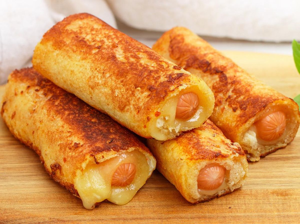 Sepiring sosis gulung roti renyah dengan taburan keju parut, disajikan bersama saus tomat