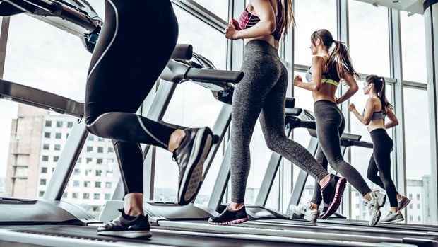 Running together. Side view of young beautiful women looking away while running on treadmill at gym.
