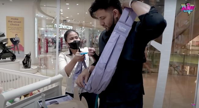 Dengan dibantu oleh pelayan di sana, Ammar tampak mencoba kain gendongan yang dipilih oleh sang istri. Gimana, sudah cocok jadi ayah 2 anak belum nih? Foto: YouTube/Aish TV