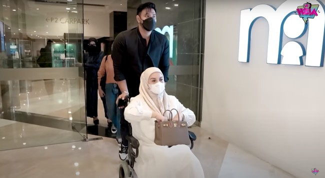 Melalui salah satu unggahan video di channel YouTube miliknya, Irish Bella dan Ammar Zoni tampak membagikan keseruan mereka ketika belanja keperluan bayi jelang kelahiran anak kedua. Sedaang hamil besar, Irish pun tampak didorong menggunakan kursi roda oleh sang suami. Foto: YouTube/Aish TV