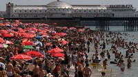 Pengunjung pantai menikmati matahari dan laut di pantai di Brighton, Inggris selatan, Minggu, (17/7/2022).