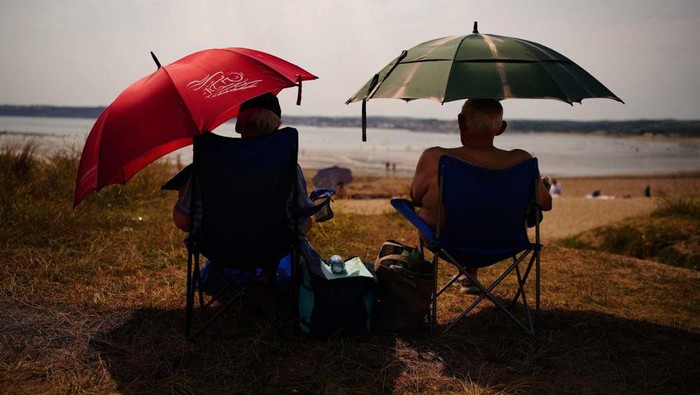 People sheltering under umbrellas from the sun in St Michaels Bay in Cornwall, England, Sunday July 17, 2022. The Met office has issued its first-ever “red warning” of extreme heat for Monday and Tuesday, when temperatures in southern England may reach 40 C (104 F) for the first time. (Ben Birchall/PA via AP)