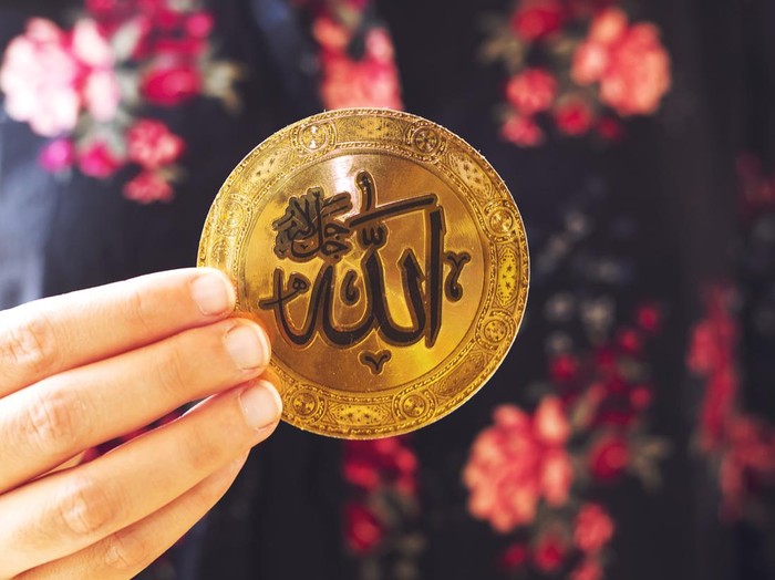 muslim woman holding a golden paper  with Arabic calligraphy of Allah (Islamic God)