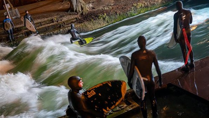 18 July 2022, Bavaria, Munich: A man surfs on the artificial wave of the Eisbach in the English Garden under floodlight late Monday evening. As illumination for their sport, the surfers have placed an LED lamp on the nearby bridge on their own initiative, so that they can still see something in the darkness. The Eisbach endurance wave on Prinzregentenstraße is a popular spot for surfers to practice their sport all year round. Photo: Peter Kneffel/dpa (Photo by Peter Kneffel/picture alliance via Getty Images)