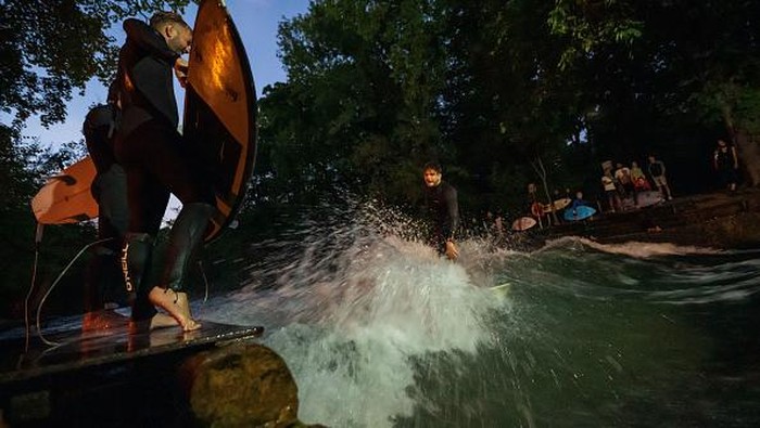 Sensasi Surfing di Tengah Kota Jerman Saat Malam Hari 18 July 2022, Bavaria, Munich: A man surfs on the artificial wave of the Eisbach in the English Garden under floodlight late Monday evening. As illumination for their sport, the surfers have placed an LED lamp on the nearby bridge on their own initiative, so that they can still see something in the darkness. The Eisbach endurance wave on PrinzregentenstraΓe is a popular spot for surfers to practice their sport all year round. Photo: Peter Kneffel/dpa (Photo by Peter Kneffel/picture alliance via Getty Images)