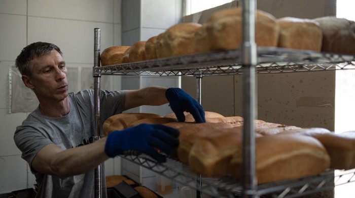 KYIV, UKRAINE - JULY 19: Good Bread bakery worker takes loafs of bread from the oven on July 19, 2022 in Kyiv, Ukraine. Good Bread bakery has been employing people with mental disabilities since its opening several years ago. Weeks after the Russian invasion, the bakery returned to work to bake bread for thousands of people in need. Now the bakery distributes nearly a 1000 loaves of bread per day for soldiers of the Armed Forces and Territorial Defense, the police, hospital patients, residents of mental hospitals, elderly people, and families with children who stayed in Kyiv, as well as the residents of the villages and towns that were destroyed during the Russian invasion. (Photo by Alexey Furman/Getty Images)