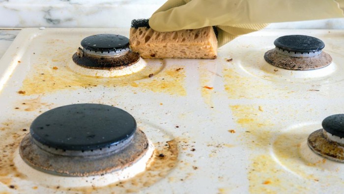 cleaning a dirty modern kitchen gas stove with a sponge