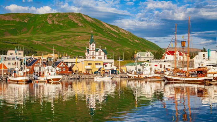 Scenic view of the historic town of Husavik in beautiful golden evening light at sunset with blue sky and clouds, north coast of Iceland