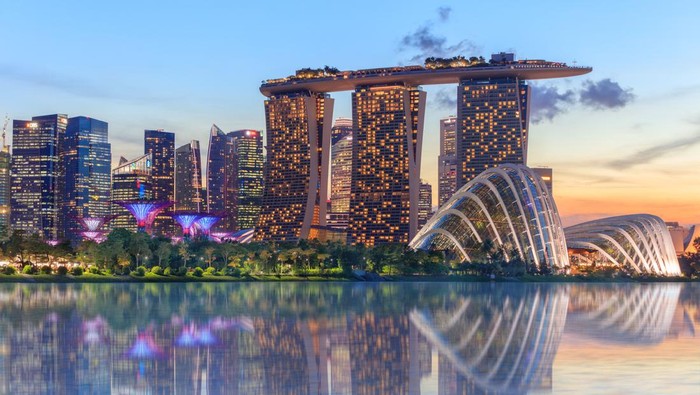 Singapore, Republic of Singapore - May 4, 2016: Supertree grove, Cloud garden greenhouse and Marina Bay Sands hotel reflecting in water at dusk with glowing lights