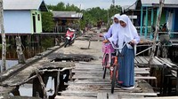 Dua orang siswa menuntun sepedanya melewati jalan rusak di Desa Igal, Indragiri Hilir, Riau.