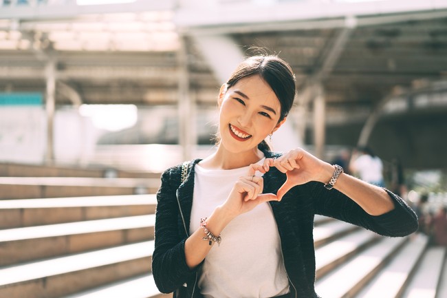 Happy smile young adult asian business single woman hand up with heart gesture. Wear silver accessory and charm for lover faith on valentine day. City people lifestyle concept.