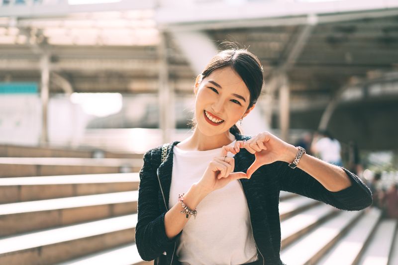 Happy smile young adult asian business single woman hand up with heart gesture. Wear silver accessory and charm for lover faith on valentine day. City people lifestyle concept.