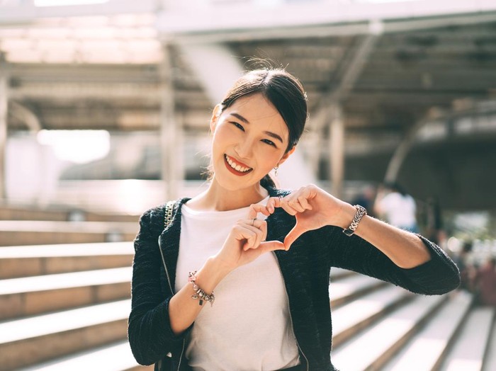 Happy smile young adult asian business single woman hand up with heart gesture. Wear silver accessory and charm for lover faith on valentine day. City people lifestyle concept.