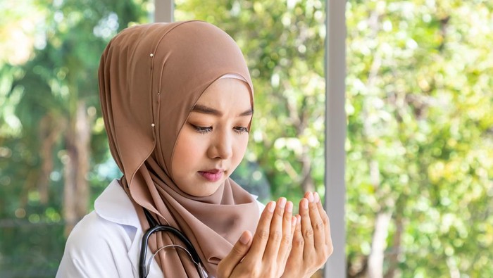 Confident beautiful Muslim female woman medical doctor standing and praying with stethoscope