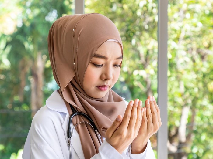Confident beautiful Muslim female woman medical doctor standing and praying with stethoscope