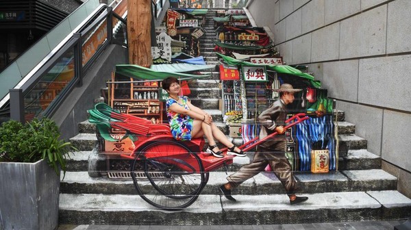 Seorang wanita di Chongqing, China, terlihat menumpang becak tradisional. Padahal wanita tersebut hanya duduk santai di anak tangga.