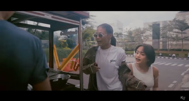 Jeje dan Bonge tampil dalam balutan busana ala street style, sama seperti gaya keduanya ketika nongkrong di stasiun BNI City. Jeje terlihat simple dengan crop top putih dan Bonge tampil lengkap dengan kaca mata hitam yang dikenakannya. Foto: YouTube/Kelvin Joshua