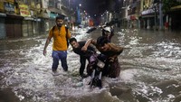 Warga mendorong sepeda motornya yang mogok akibat banjir, Minggu (24/7).