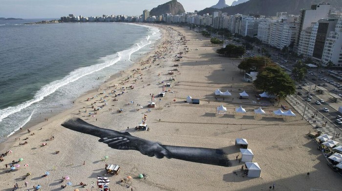 Lukisan Raksasa Lambang Kebersamaan Mejeng di Pantai Brasil A land-art fresco made with biodegradable paint of charcoal, chalk, water and milk proteins, by French-Swiss artist Saype, covers Copacabana beach as part of the artist's worldwide project titled Beyond Walls in Rio de Janeiro, Brazil, Friday, July 15, 2022. The artist said he is creating a symbolic human chain around the world with the aim of promoting togetherness, kindness and openness to the world. (AP Photo/Silvia Izquierdo)