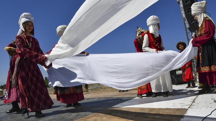 A Kyrgyz woman lays out carpets in front of yurt, traditional Kyrgyz houses during the Ak-Moor Fest Ethno-festival in Ornok, a resort village on the northern shore of Lake Issyk-Kul, 207 kilometers (129 miles) east of Bishkek, Kyrgyzstan, Saturday, July 23, 2022. On the shore of one of the world's largest lakes, high up in Kyrgyzstan's Tian Shan mountains, models strutted and sashayed in outfits mixing the ancient and modern at the World Nomads Fashion festival. (AP Photo/Vladimir Voronin)