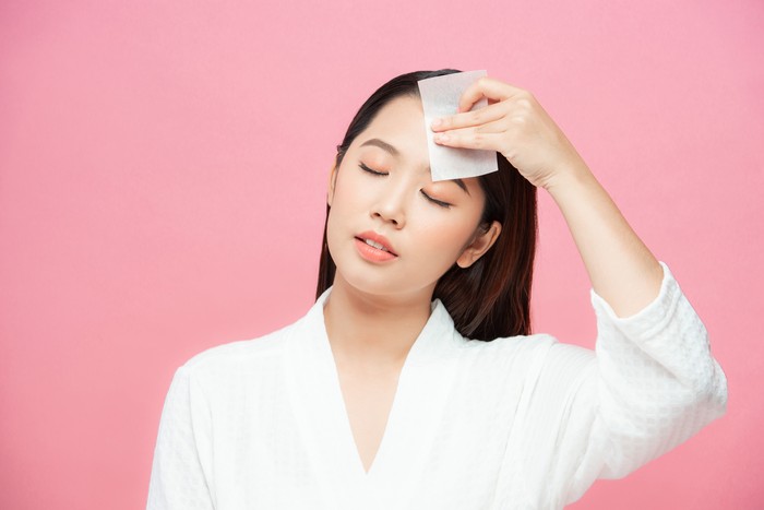 Ilustrasi Skincare Kulit Berminyak Woman using facial oil blotting paper. Photo of woman with perfect makeup on pink background. Beauty concept