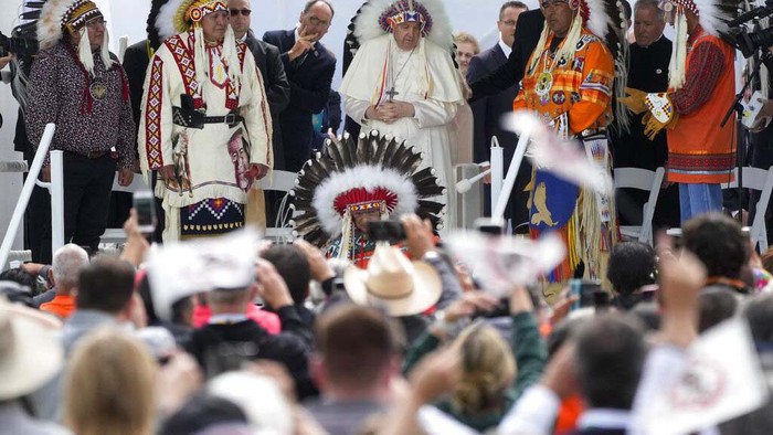 Pope Francis dons a headdress during a visit with Indigenous peoples at Maskwaci, the former Ermineskin Residential School, Monday, July 25, 2022, in Maskwacis, Alberta. Pope Francis traveled to Canada to apologize to Indigenous peoples for the abuses committed by Catholic missionaries in the country's notorious residential schools. (AP Photo/Eric Gay)