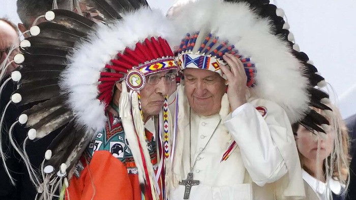 Kunjungi Kanada, Paus Fransiskus Pakai Penutup Kepala Pribumi Pope Francis dons a headdress during a visit with Indigenous peoples at Maskwaci, the former Ermineskin Residential School, Monday, July 25, 2022, in Maskwacis, Alberta. Pope Francis traveled to Canada to apologize to Indigenous peoples for the abuses committed by Catholic missionaries in the country's notorious residential schools. (AP Photo/Eric Gay)