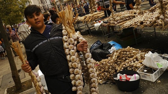Pasar di Spanyol Ini Cuma Jual Bawang Putih A boy carries strips of garlics during the garlics fair in Vitoria, northern Spain, Monday, July 25, 2022. Every year a traditional garlic market is set on the Saint James patron day in Vitoria gathering producers of all around Spain. (AP Photo/Alvaro Barrientos)