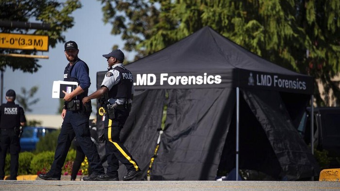 A police officer stands near a RCMP vehicle with bullet holes in the windshield and driver's side window at the scene of a shooting in Langley, British Columbia, Monday, July 25, 2022. (Darryl Dyck/The Canadian Press via AP)
