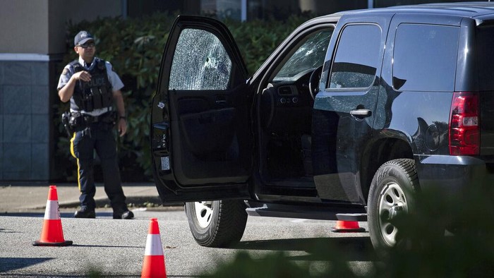 A police officer stands near a RCMP vehicle with bullet holes in the windshield and driver's side window at the scene of a shooting in Langley, British Columbia, Monday, July 25, 2022. (Darryl Dyck/The Canadian Press via AP)