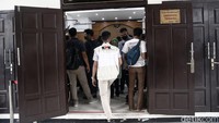 Petugas KPK terlihat mengenakan rompi bertuliskan KPK dan berwarna krem. Mereka memantau di sekitar ruang sidang.