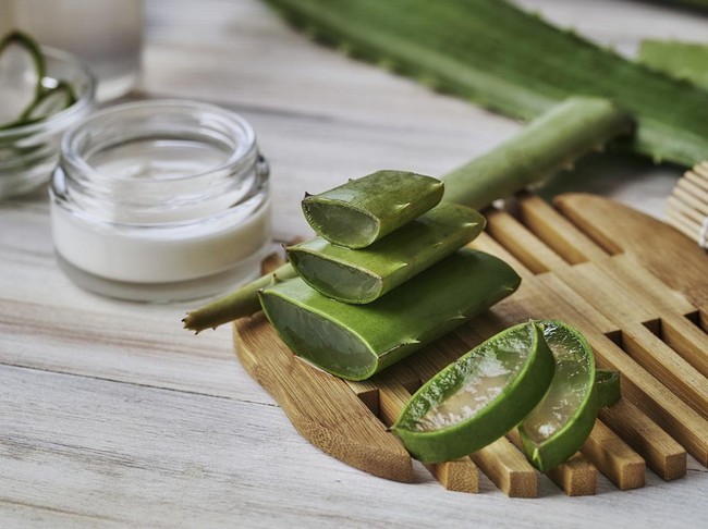 Aloe vera slices and moisturizer on a wooden table. Beauty treatment concepts