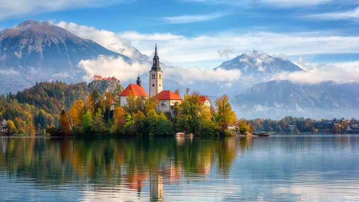 Famous alpine Bled lake (Blejsko jezero) in Slovenia, amazing autumn landscape. Scenic view of the lake, island with church, Bled castle, mountains and blue sky with clouds, outdoor travel background