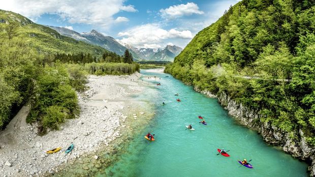 Group of people kayaking on the river Soča in Slovenia Europe. Scenic nature, with turquoise water river, surrounded with bushy forest in the summer time.