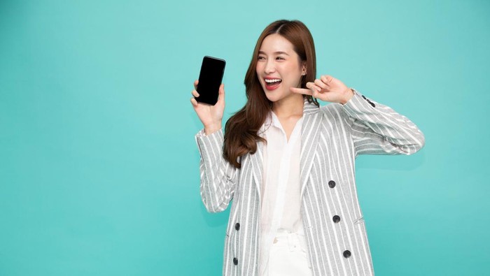 Portrait of Southeast Asian business woman showing or presenting mobile phone application on hand isolated on green background, One person of horizontal orientation, Blank screen smartphone concept