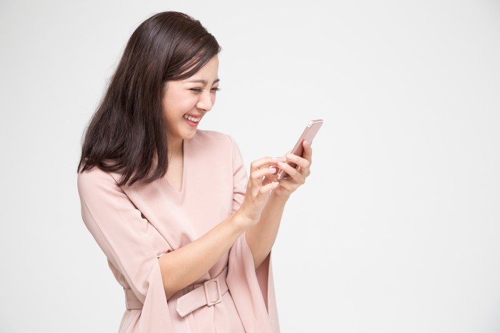 Cheerful young Asian woman using smartphone and receiving good news from the message on mobile chat application over white background