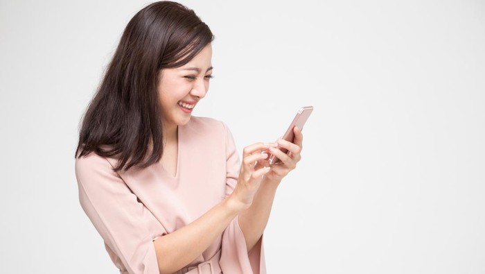 Cheerful young Asian woman using smartphone and receiving good news from the message on mobile chat application over white background