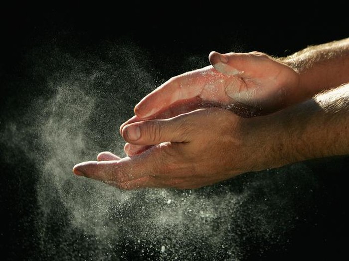A sportsman chalks his hands in front of a black background