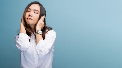 Woman covering her ears and standing isolated over blue background