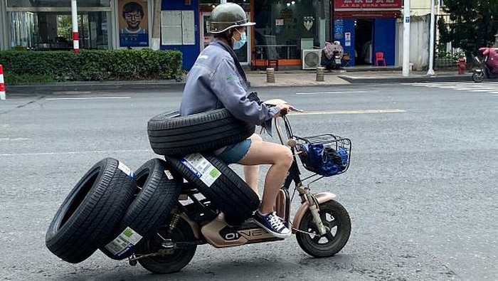 Motor Listrik Ini Punya '6 Roda', 1nya Dipinggang HUAI'AN, CHINA - JULY 26, 2022 - A female electric driver drives slowly with four car tires and a car tire around her waist on a street in Huai 'an, East China's Jiangsu Province, China, July 26, 2022. (Photo credit should read CFOTO/Future Publishing via Getty Images)